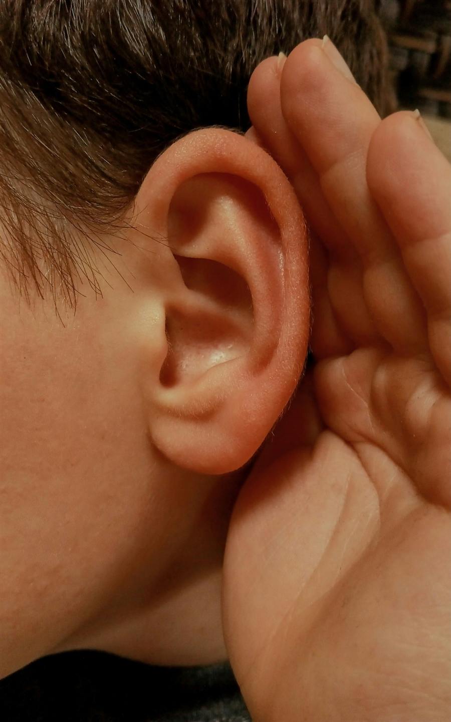 Main en creux derrière l'oreille, attentive à écouter